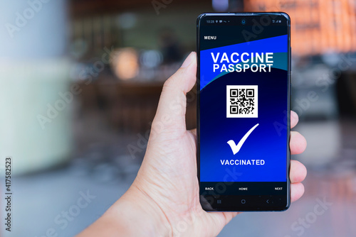 Smartphone displaying a valid digital vaccination certificate for COVID-19 in male's hand, public area background. Vaccination, disease immunity passport, health and safty travel concepts