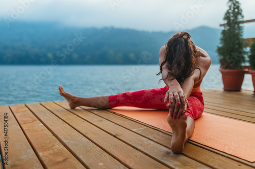 Woman practicing yoga poses in nature at lake pier