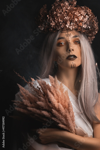 white girl in the image of the deity of autumn, with a wreath on her head made of dry leaves, in the hands of a girl a bouquet of dried flowers, on her face makeup in the Scandinavian style