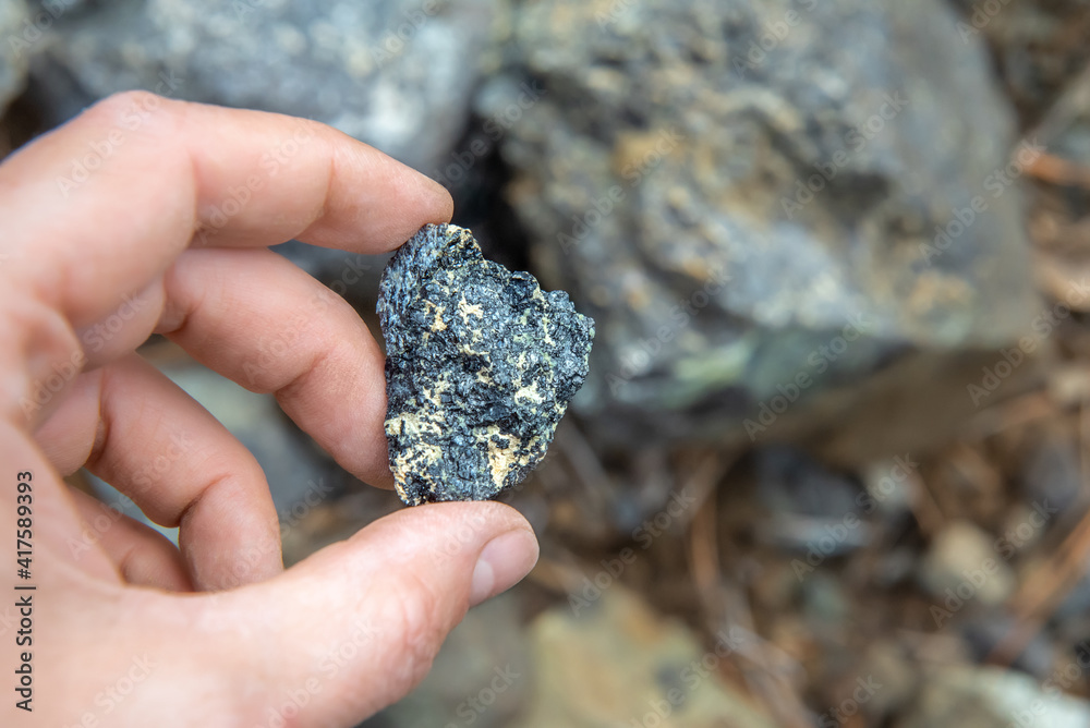 Chromite ore in hand, selective focus. Piece of natural mineral over rocks background