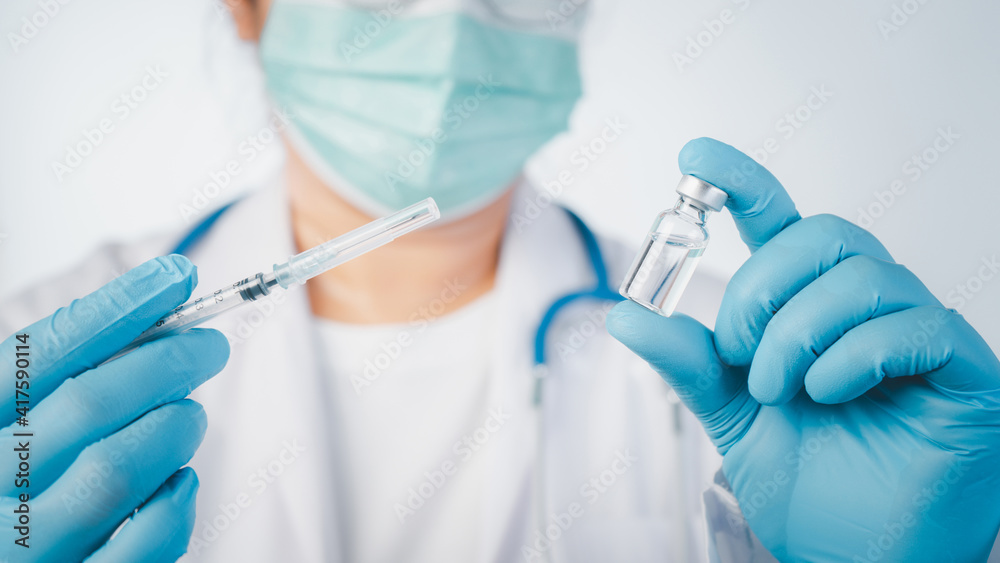 Doctor wear hand in blue gloves holding a syringe with liquid vaccines,Concept covid-19 corona virus. Doctor wear hand in blue gloves holding a syringe with liquid vaccines,Concept covid-19 corona virus.