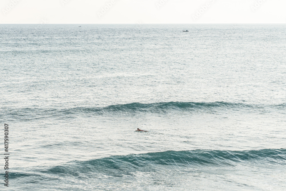 Obraz premium Surfer pośród fal na oceanie na tle zachodu słońca.