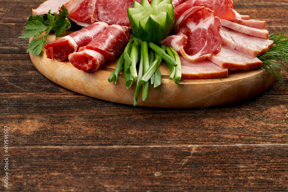 Sliced pork loin and carbonado with onion feathers on a wooden round board on a textured table. Still life with copy space for text Sliced pork loin and carbonado with onion feathers on a wooden round board on a textured table. Still life with copy space for text