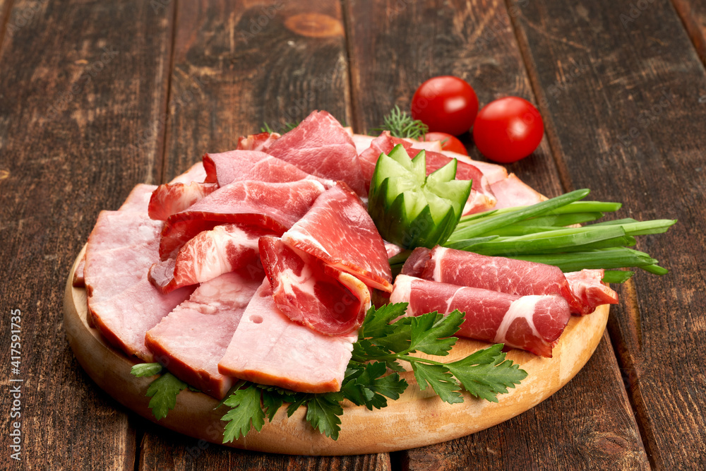 Ham with tomatoes and herbs on a wooden board, wooden background.