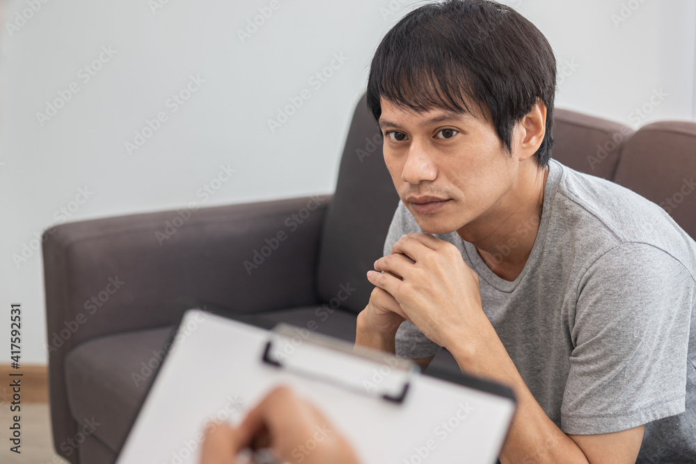Young asian man, male has mental symptoms which must have been therapy and stress, sitting on couch to consult to psychologist during the session taking notes to find out how to treat the therapist. Young asian man, male has mental symptoms which must have been therapy and stress, sitting on couch to consult to psychologist during the session taking notes to find out how to treat the therapist.
