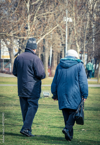 Old couple strolling or walking on the green grass in the park. © Cristi