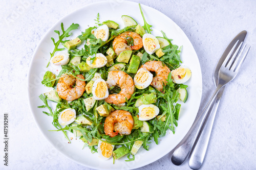 Salad with shrimp, avocado, cucumber, quail eggs and arugula. Mediterranean traditional cuisine. Close-up.