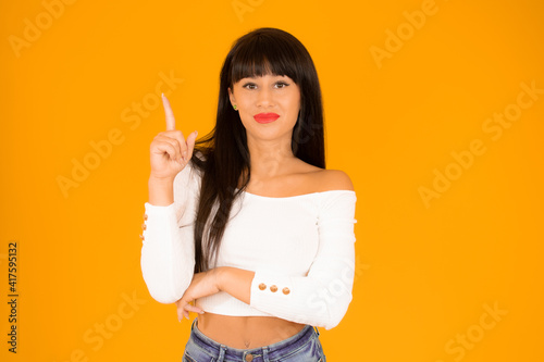 Portrait of a happy young woman dressed in casual clothes pointing finger up at copy space isolated over orange background