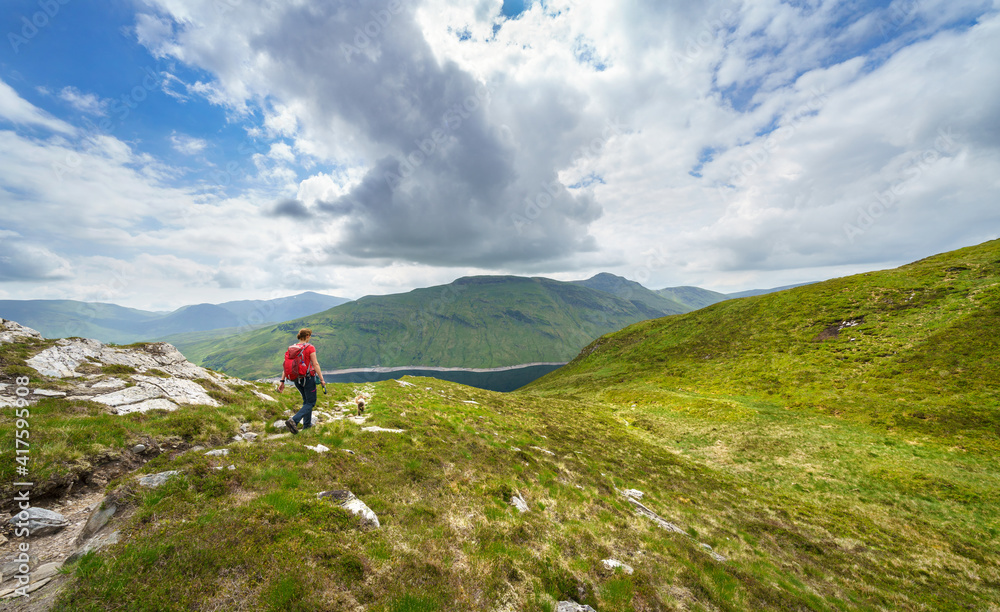 A female hiker descending the summit Meall a Phuill towards Loch an Daimh in the Scottish Highland mountains, UK landscapes.