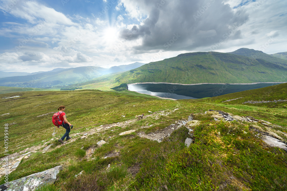 A female hiker descending the summit Meall a Phuill towards Loch an Daimh in the Scottish Highland mountains, UK landscapes.