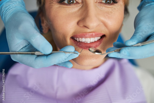 Hands holding dental probe and intraoral mirror near woman teeth