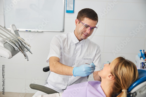 Friendly doctor in face shield looking inside woman mouth