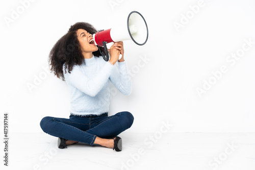 Young african american woman sitting on the floor shouting through a megaphone