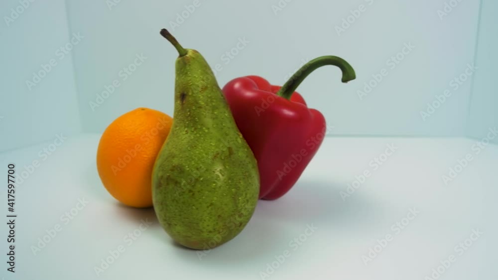 Fresh big green pear, red sweet bell pepper, juicy orange rotates slowly on a light blue background, healthy food concept, close up shot, camera rotate right Fresh big green pear, red sweet bell pepper, juicy orange rotates slowly on a light blue background, healthy food concept, close up shot, camera rotate right