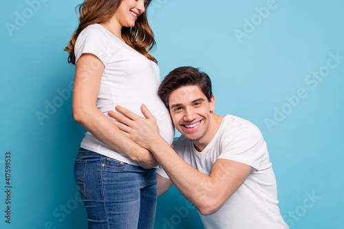 Cropped photo of optimistic couple man hug listen baby in stomach wear white t-shirts isolated on teal color background