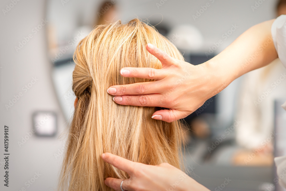 Fototapeta premium Close up of female hairdresser styling blonde hair of a young woman in a beauty salon