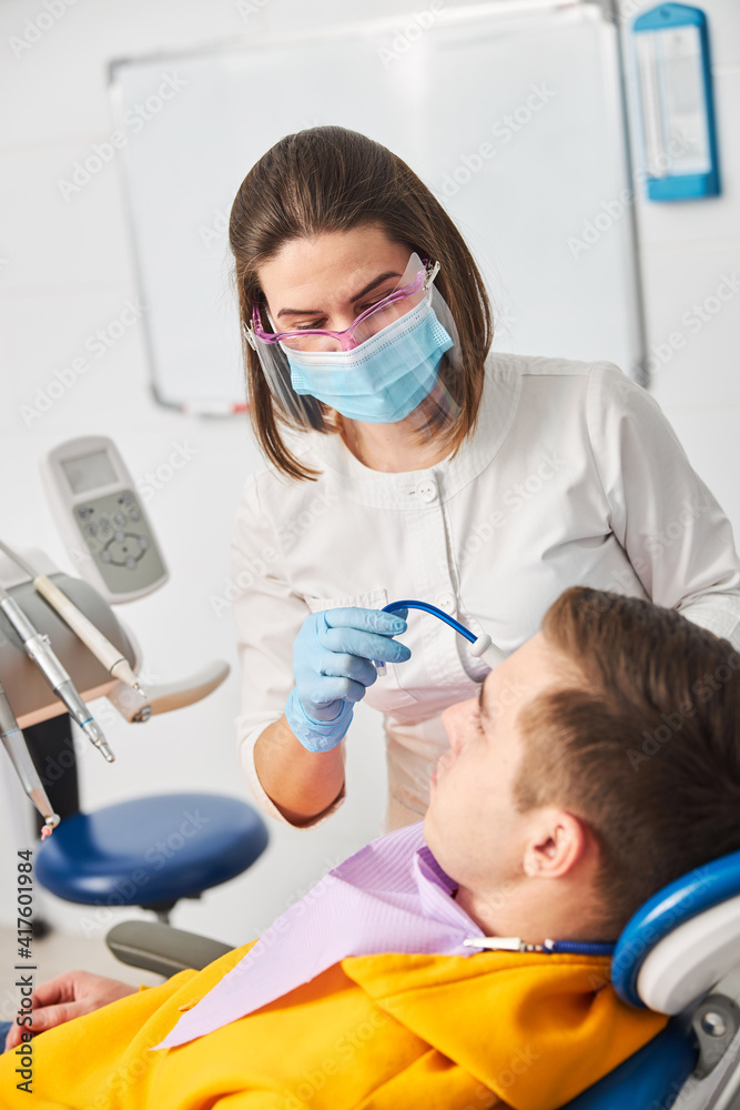 Stomatologist directing saliva ejector to man mouth Stomatologist directing saliva ejector to man mouth