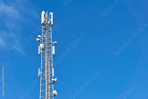 4G and 5G transmitters on a telecommunications tower. Cellular base station with white transmitting antennas on a high pole against a blue sky. Image with copy space. 