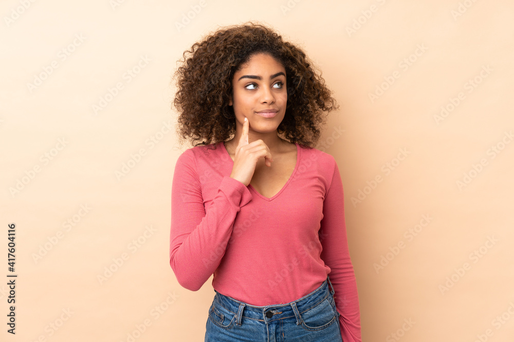 Young African American woman isolated on beige background thinking an idea while looking up