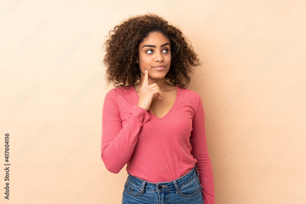 Young African American woman isolated on beige background thinking an idea while looking up Young African American woman isolated on beige background thinking an idea while looking up