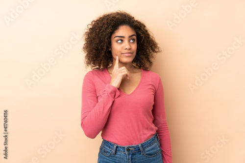 Young African American woman isolated on beige background thinking an idea while looking up
