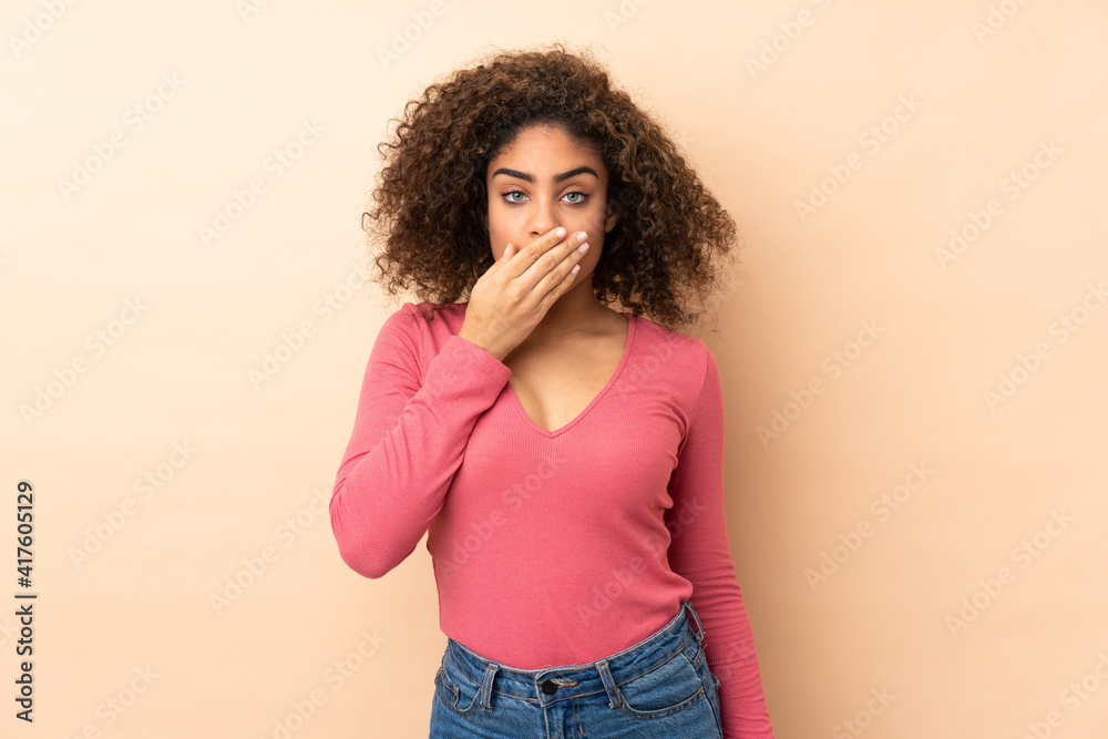 Young African American woman isolated on beige background covering mouth with hand Young African American woman isolated on beige background covering mouth with hand