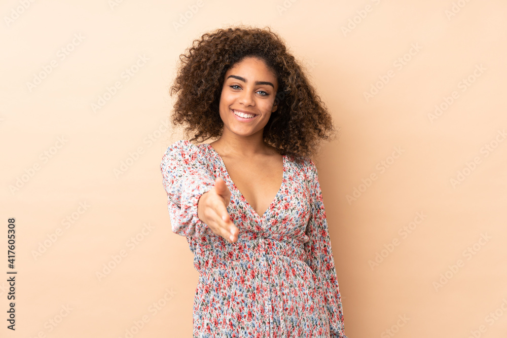 Young African American woman isolated on beige background shaking hands for closing a good deal Young African American woman isolated on beige background shaking hands for closing a good deal