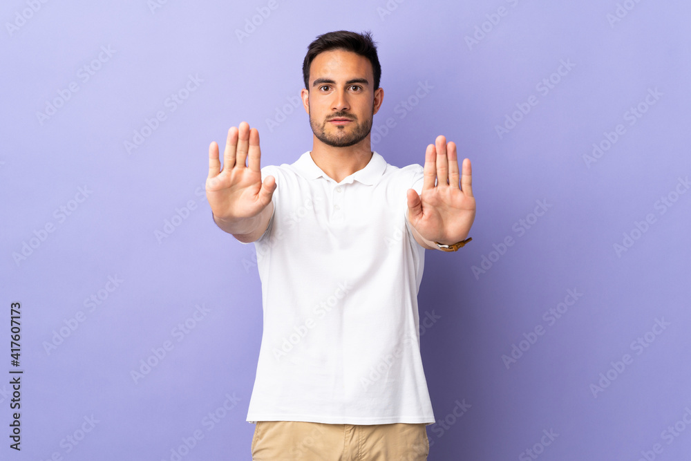 Young handsome man isolated on purple background making stop gesture and disappointed Young handsome man isolated on purple background making stop gesture and disappointed