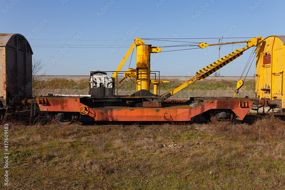 Old yellow cargo crane wagon on abandoned train tracks in the field
