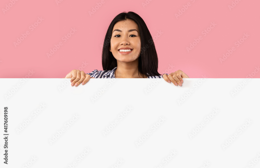 Asian woman hiding behind blank white advertising billboard Asian woman hiding behind blank white advertising billboard