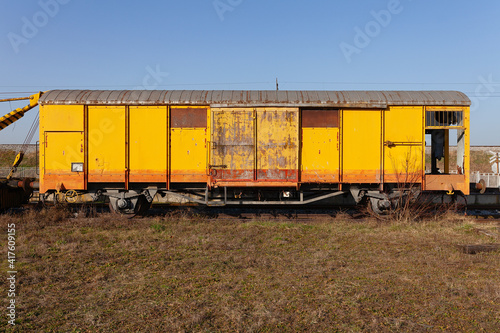 Old yellow cargo train wagon, grungy and weathered on the abandoned train tracks in field