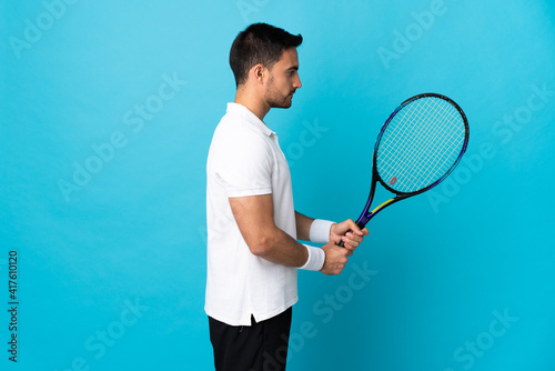 Young handsome man isolated on blue background playing tennis