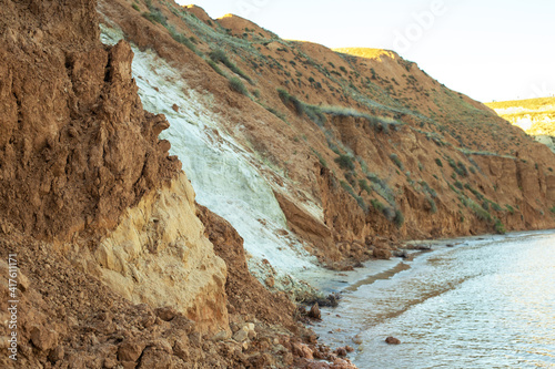 Coast landscape with white sand wall and brown layers of different clay. Sea or river coast with multicolored ground wall.