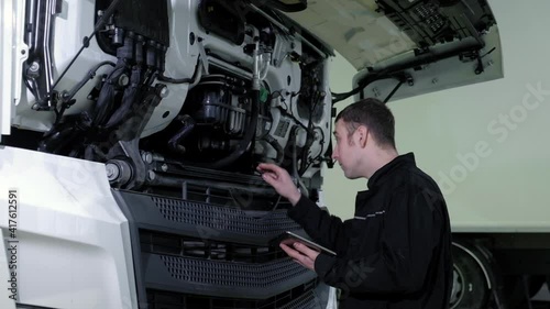 Repair diagnostics and maintenance of cars in service center. chief mechanical engineer in uniform stands next to truck uses tablet to search for errors and breakdowns and writes data to the computer