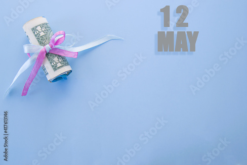 calendar date on blue background with rolled up dollar bills pinned by blue and pink ribbon with copy space. May 12 is the twelfth day of the month