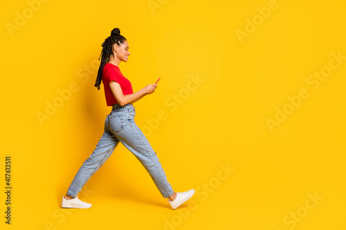 Full length body size profile side view of focused cheerful girl going using gadget 5g app smm isolated bright yellow color background