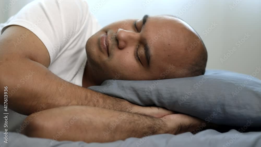 An Asian bald man around the age of 30 in a white T-shirt is sleeping on his side on a blue mattress and pillows. He slept at home until morning. An Asian bald man around the age of 30 in a white T-shirt is sleeping on his side on a blue mattress and pillows. He slept at home until morning.