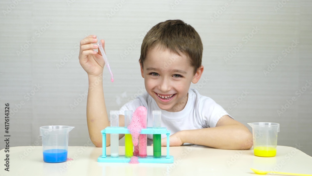 A happy child conducts experiments with chemicals by mixing them in a test tube. The boy laughs as he looks at the foam reaction in the test tube. A happy child conducts experiments with chemicals by mixing them in a test tube. The boy laughs as he looks at the foam reaction in the test tube.