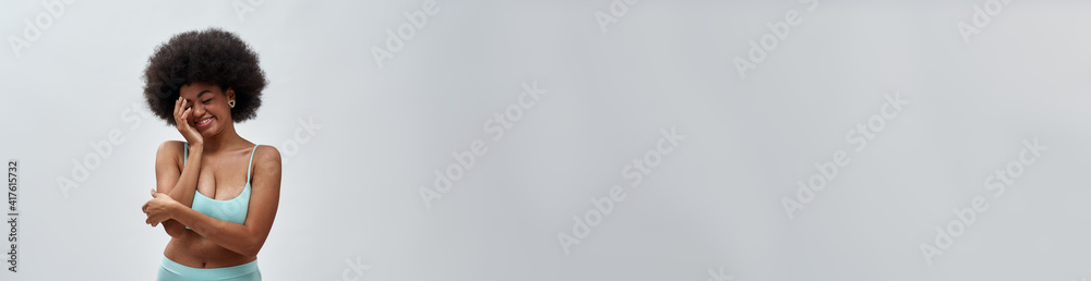 Happy voluptuous young woman with afro hair style wearing blue underwear looking shy, posing isolated over light background Happy voluptuous young woman with afro hair style wearing blue underwear looking shy, posing isolated over light background