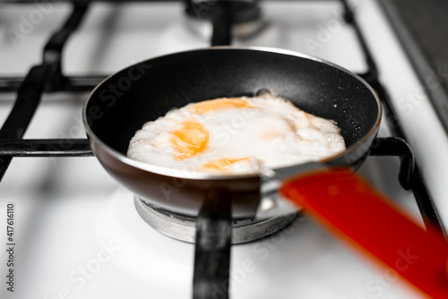 Fried eggs in frying pan, close-up. Small frying pan standing on gas stove, indoors. Selective focus. Morning breakfast concept