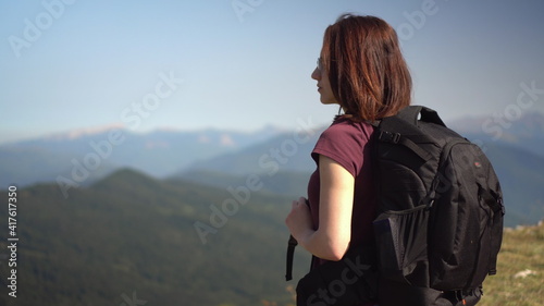 Young woman in glasses with a backpack looks at the mountain range.
