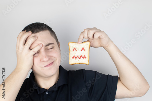 Conceptually about gluten intolerance. The man holds in his hand a piece of bread on which an angry expression is painted. Celiac disease, fear of cereals, manifestation of allergies photo