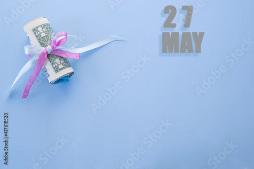 calendar date on blue background with rolled up dollar bills pinned by blue and pink ribbon with copy space. May 27 is the twenty-seventh day of the month