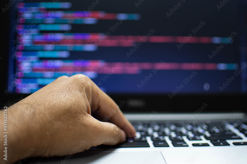 The programmer's hand is writing the source code. Programmers write programs for use with internet business services. The programming code displayed on the laptop screen. Closeup, Blurred background The programmer's hand is writing the source code. Programmers write programs for use with internet business services. The programming code displayed on the laptop screen. Closeup, Blurred background