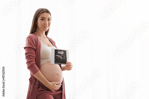 Cute Pregnant Lady Posing With Baby Sonography Photo Near Window At Home