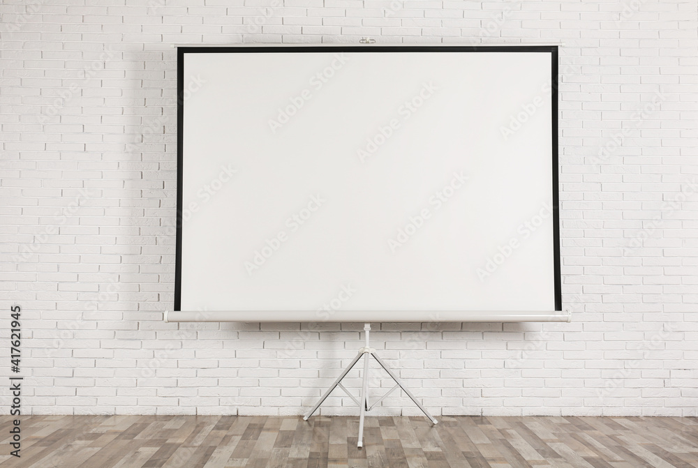 Blank projection screen near white brick wall indoors. Space for design