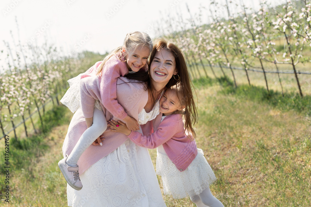 Happy family in the Apple orchard. Mom and two twin daughters have fun and hug Happy family in the Apple orchard. Mom and two twin daughters have fun and hug