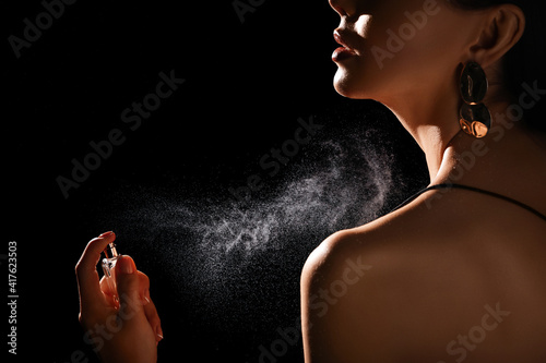 Woman spraying luxury perfume on black background, closeup photo