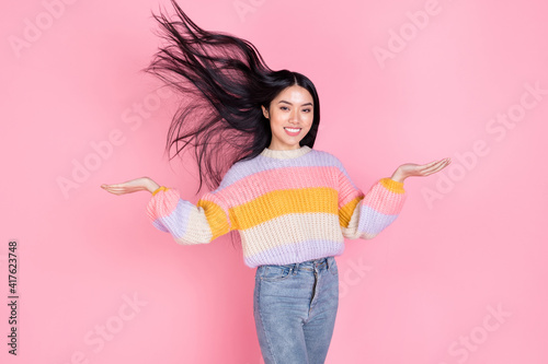 Photo of young smiling beautiful korean girl with flying hair promoting hair care treatment isolated on pink color background