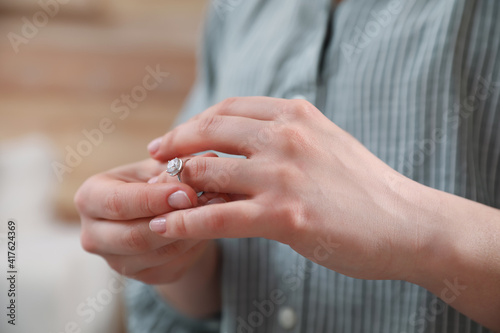 Woman taking off wedding ring indoors, closeup. Divorce concept